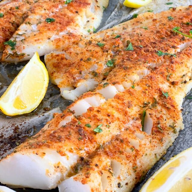 two pieces of fish with lemons and parsley on the side in a pan