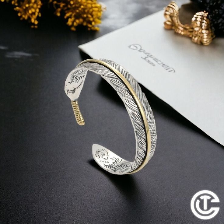 a gold and silver bracelet on top of a black table next to a flower vase