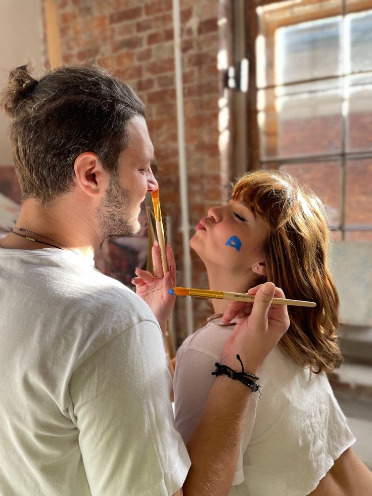 a man and woman standing next to each other with paint on their faces while holding sticks