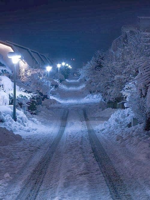 a snowy street at night with snow on the ground and lights in the dark above