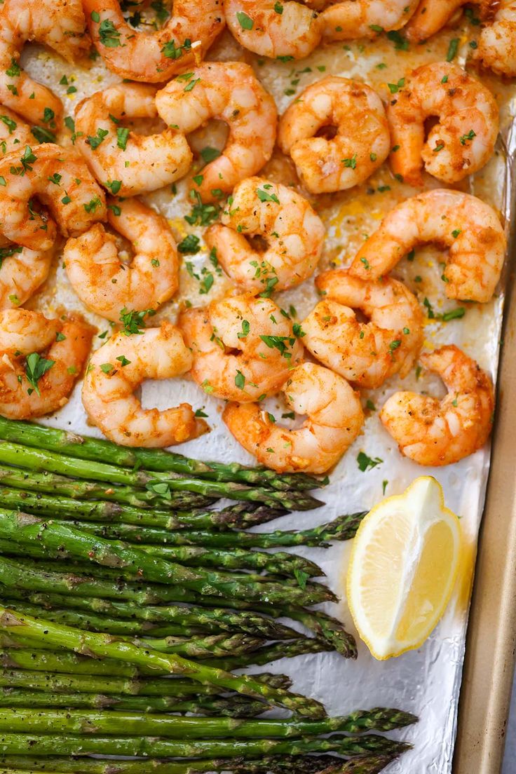 shrimp and asparagus on a baking sheet with lemon wedges