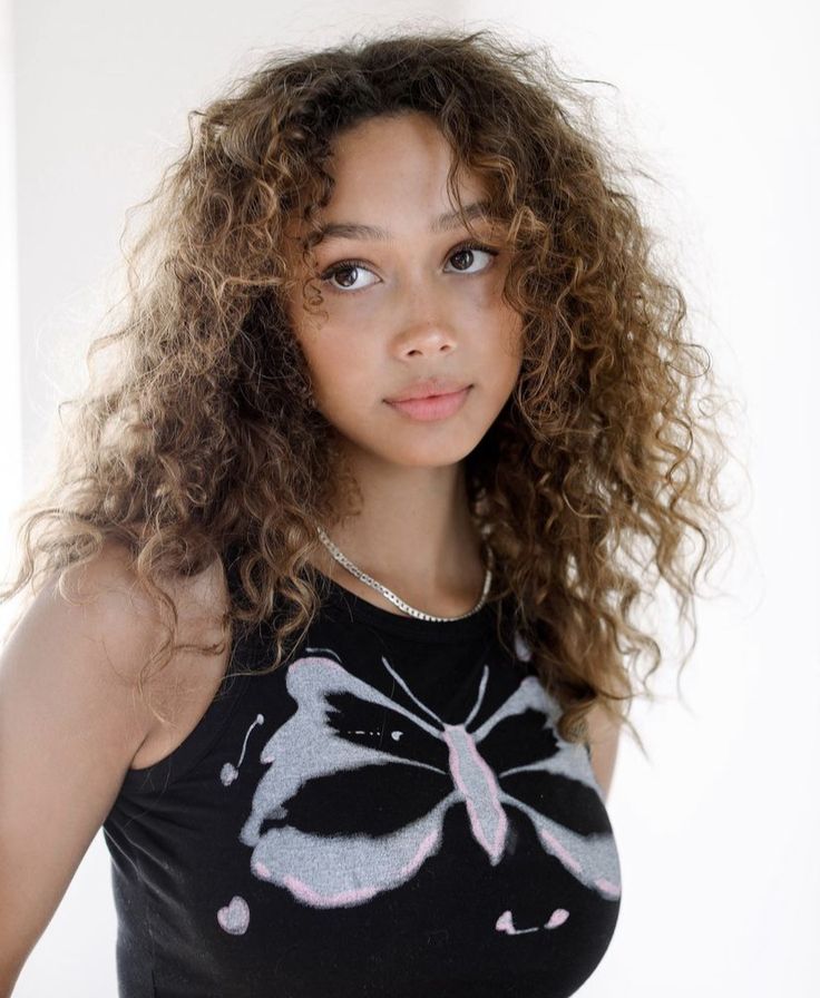 a close up of a person wearing a shirt with flowers on it and long curly hair