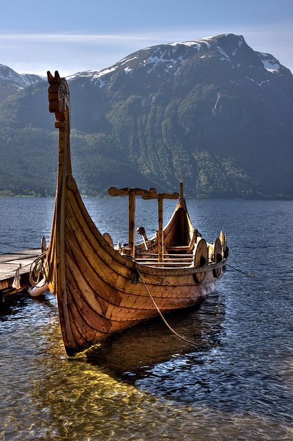 an old wooden boat sitting on top of a body of water next to snow covered mountains