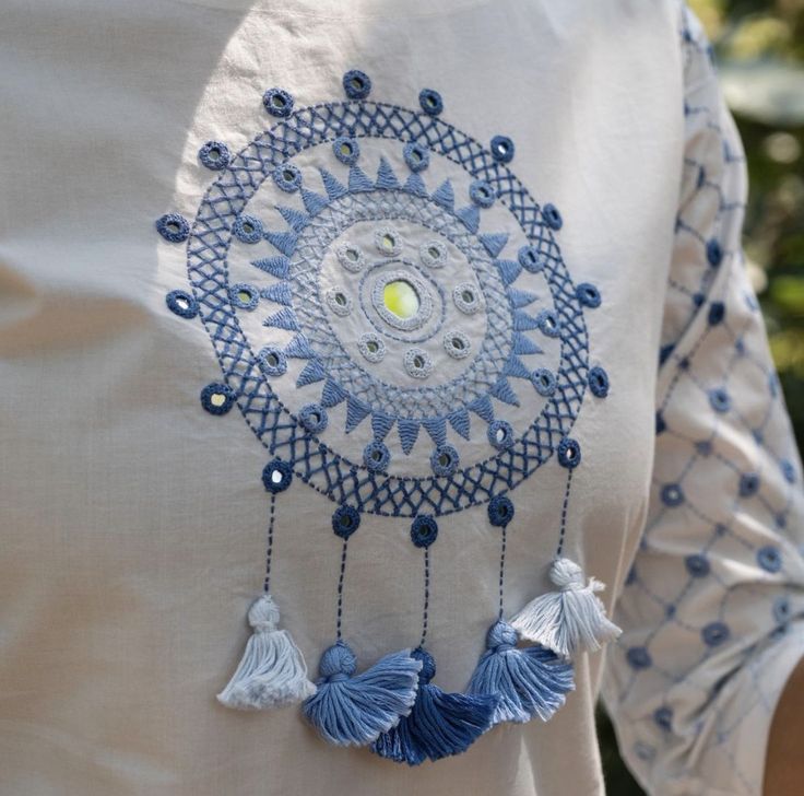 a woman's white shirt with blue tassels and beads on the back