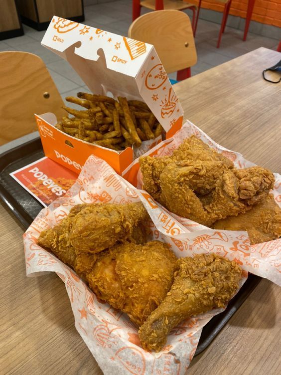 fried chicken and french fries on a tray at a fast food restaurant, with a box of fries in the background