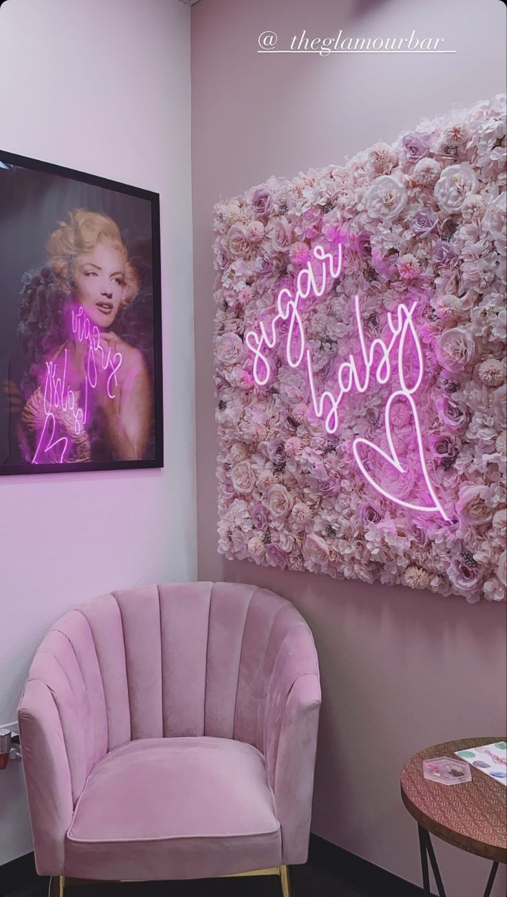 a pink chair sitting in front of a painting on the wall next to a table