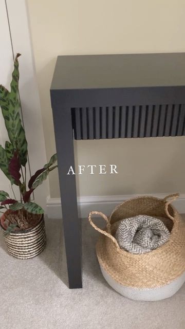 a small table with a basket under it next to a potted plant on the floor