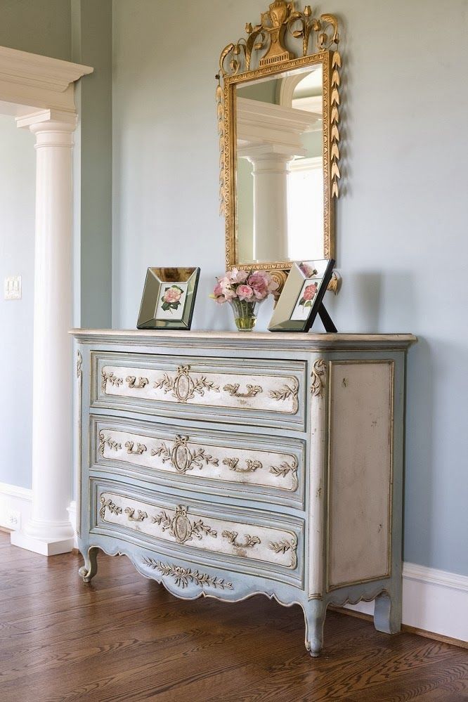 an antique dresser with flowers and pictures on it in front of a large framed mirror