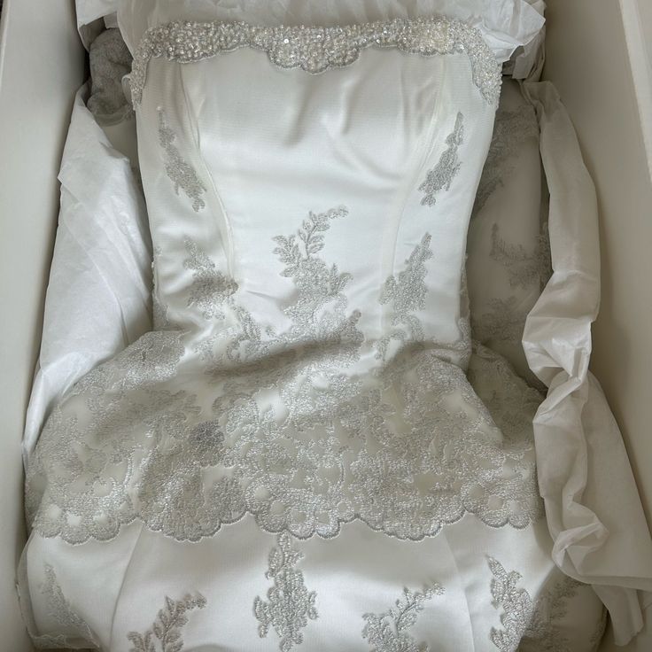 a white dress with silver lace on it in a box next to a pillow and blanket