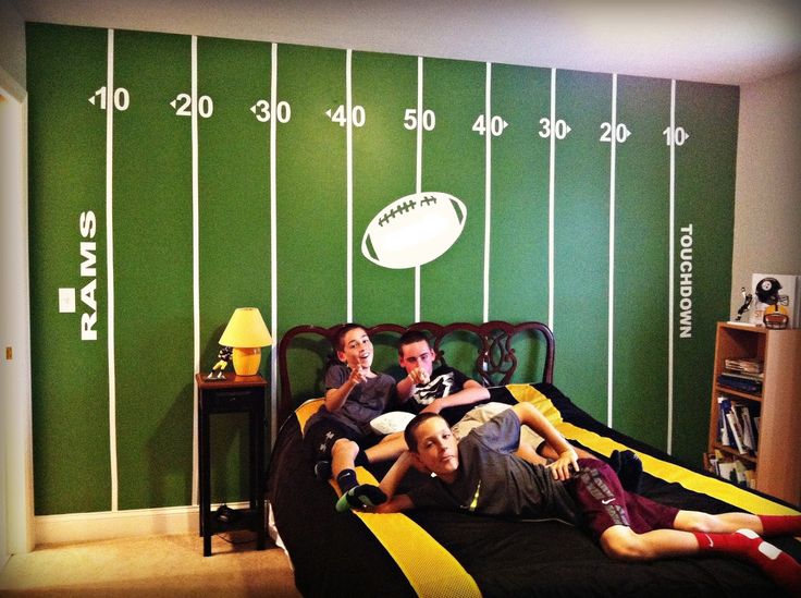 three people laying on a bed in front of a wall with footballs painted on it