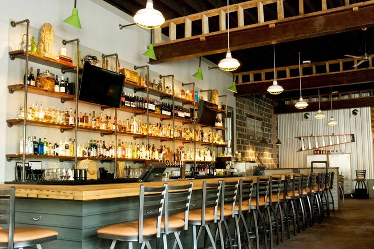 a bar with lots of bottles on the shelves and chairs in front of it,