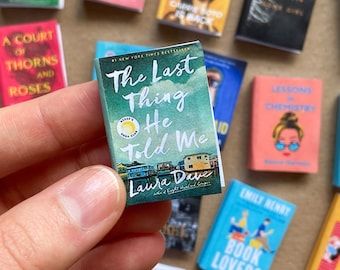 a hand holding a tiny book in front of a wall of small children's books