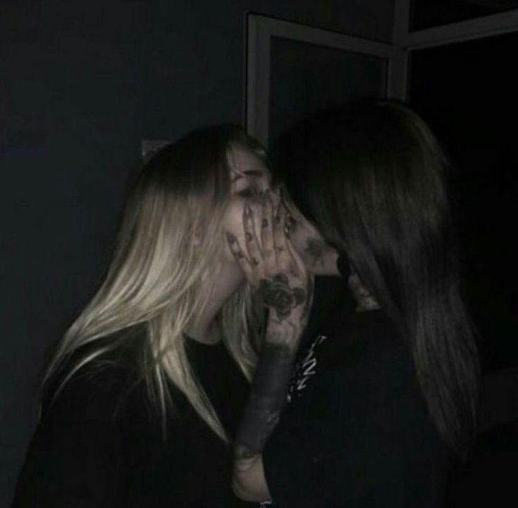 two women are kissing in the dark with their faces covered by tattoos and piercings