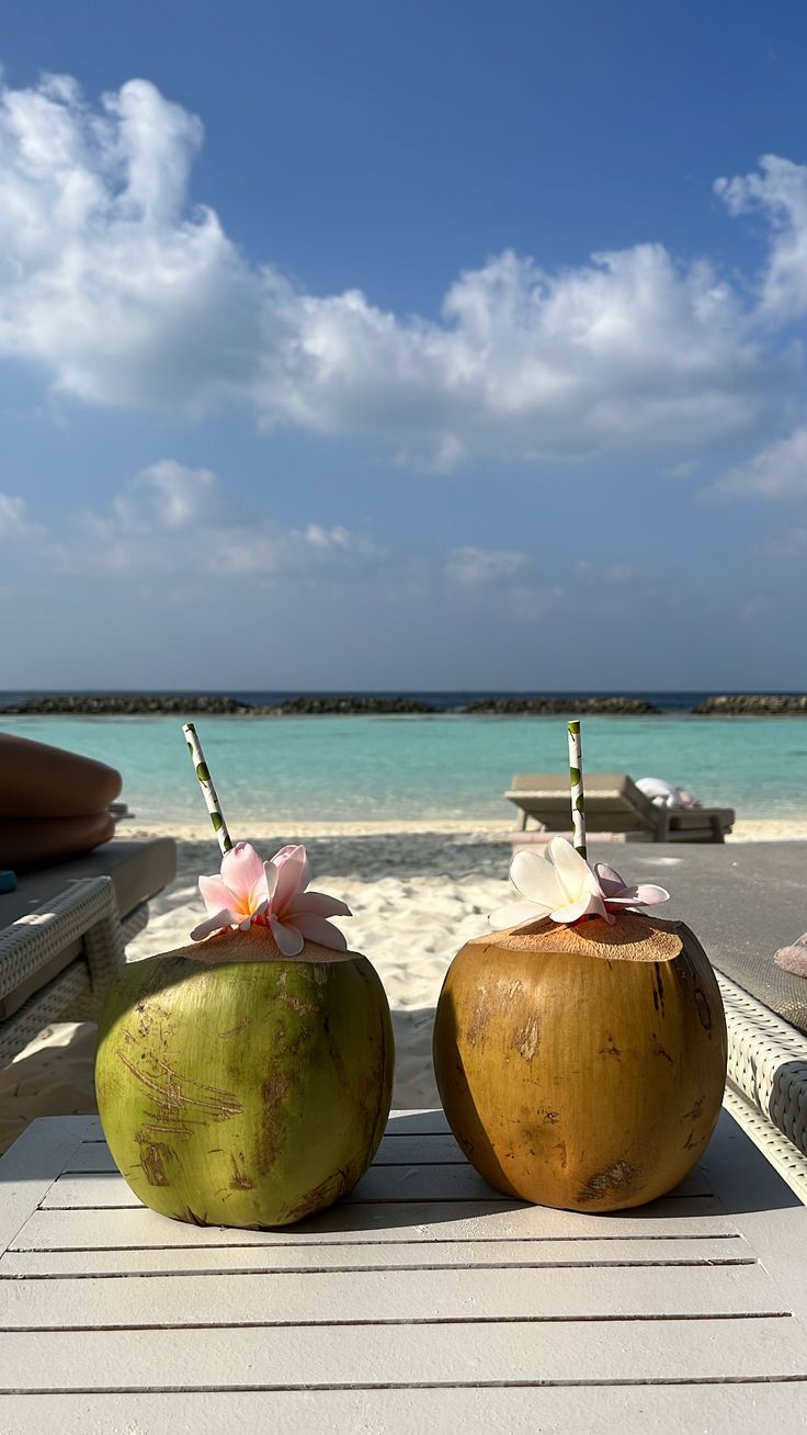 two coconuts sitting on top of a wooden table next to the ocean and beach