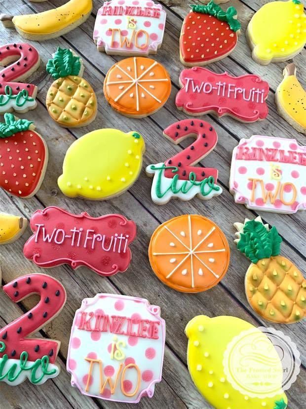 some decorated cookies sitting on top of a wooden table next to fruit and number two