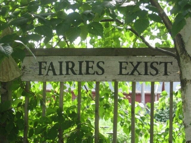 a sign that is on the side of a wooden fence in front of some trees