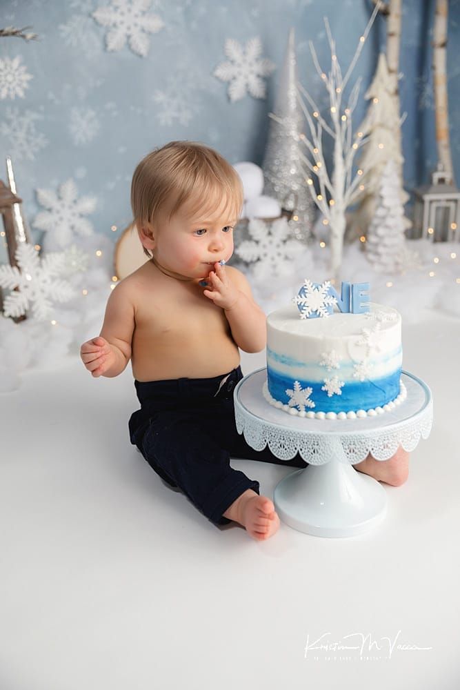 a baby sitting in front of a cake on a table with snowflakes behind it