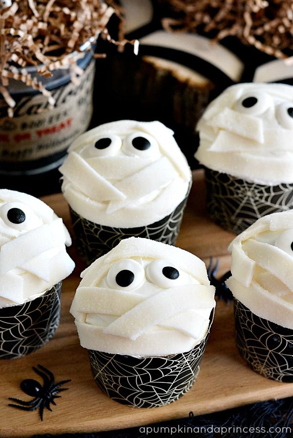 halloween cupcakes decorated with white frosting and black sprinkles on a wooden board