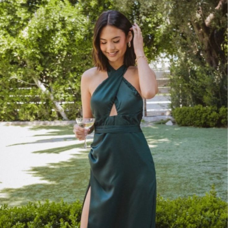 a woman in a long green dress holding a wine glass and looking at the camera