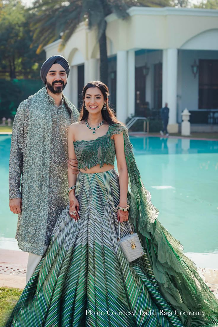 two people standing next to each other in front of a pool wearing green and blue outfits