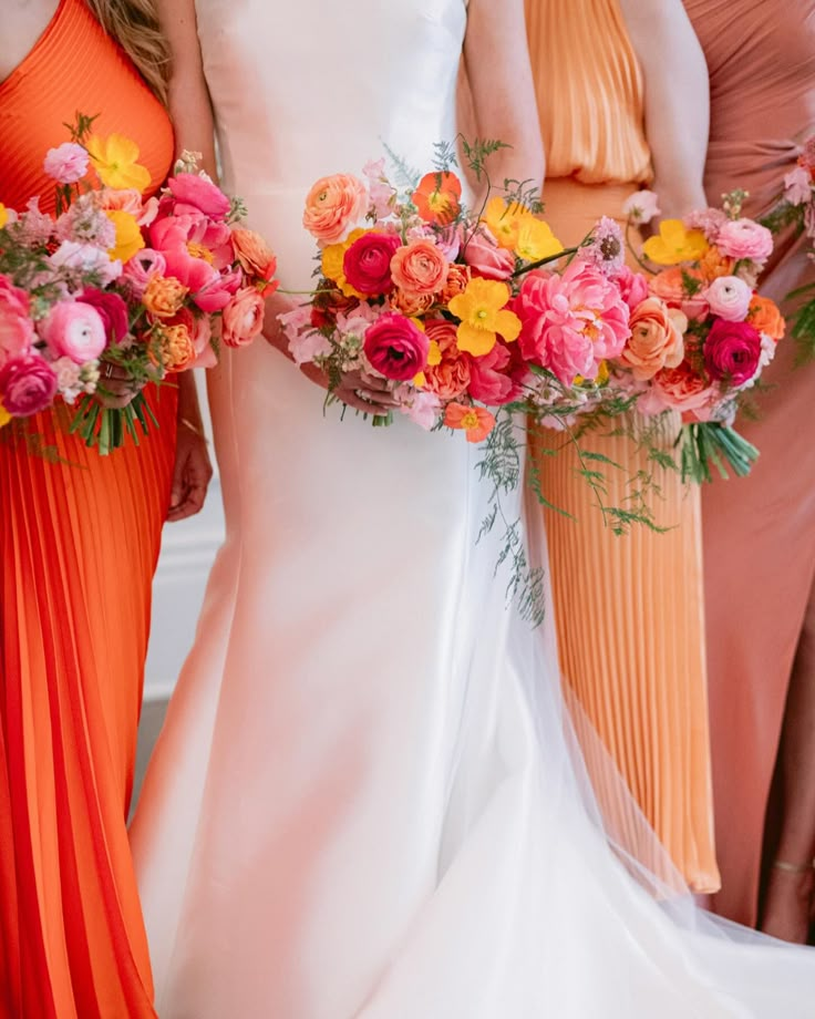 bridesmaids in orange and pink dresses holding bouquets with flowers on the side