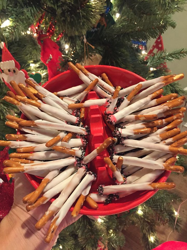 a person holding a red bowl full of pretzels in front of a christmas tree