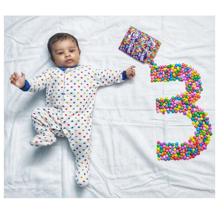 a baby laying on top of a bed next to a number 3 made out of candy