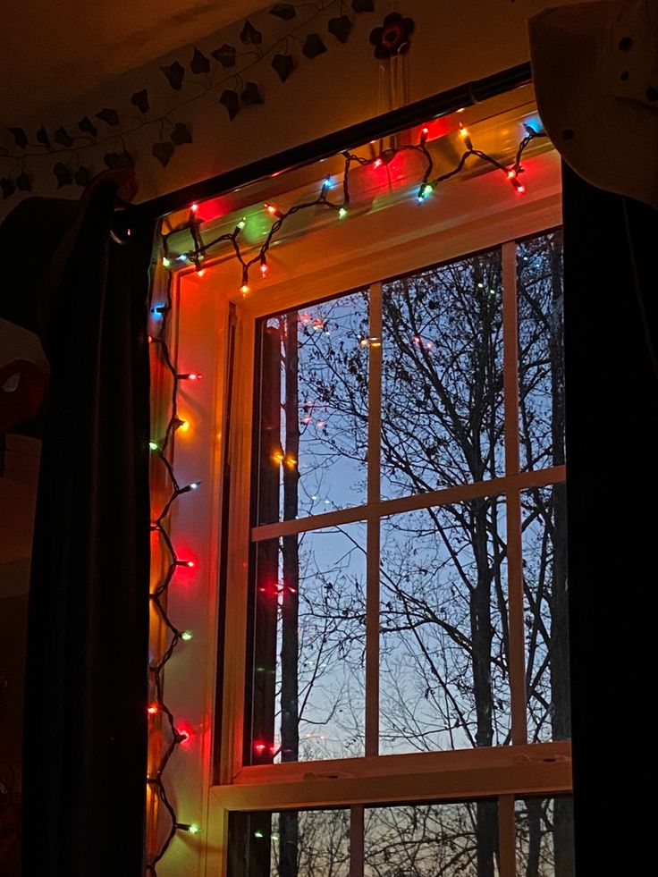 an open window with christmas lights hanging from it's sides and trees in the background