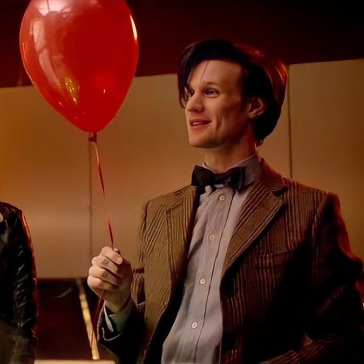 a man holding a red balloon in his right hand and wearing a bow tie, standing next to another man