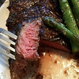 a piece of steak and asparagus on a white plate with a silver fork