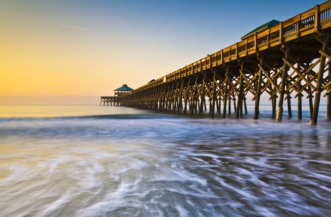 a long pier stretches out into the ocean at sunset with waves crashing in front of it