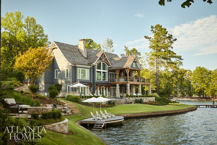 a large house sitting on top of a lush green hillside next to a lake filled with lots of trees