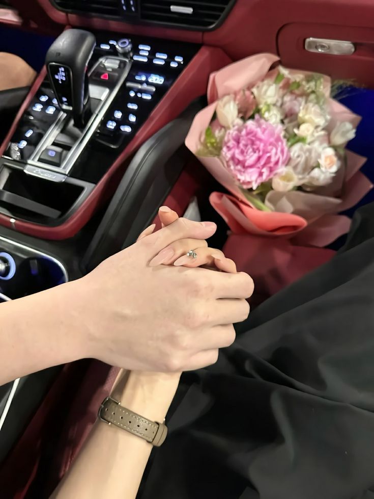 two people holding hands in the front seat of a car with flowers on the dashboard