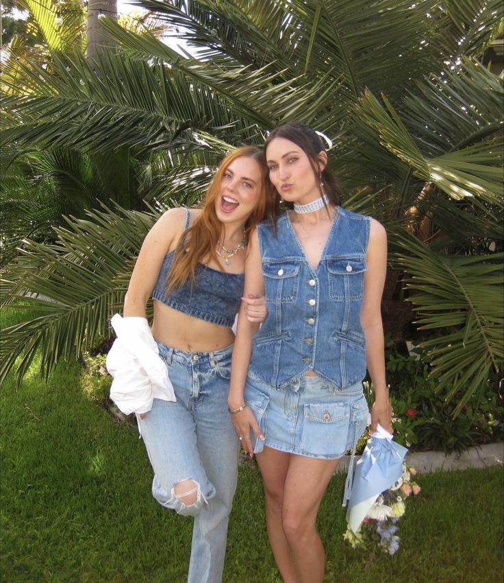 two young women standing next to each other in front of palm trees and grass,