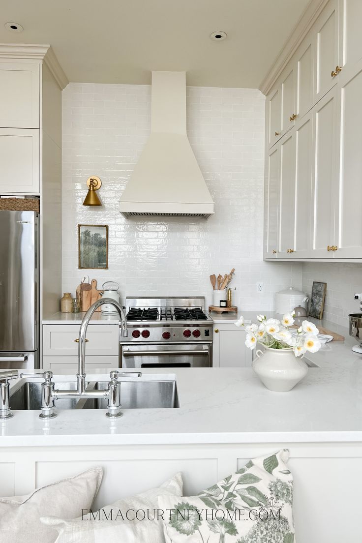 a white kitchen with stainless steel appliances and flowers in a bowl on the counter top