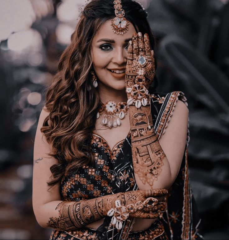 a woman in a black and gold outfit holding her hands up to her face with hendi