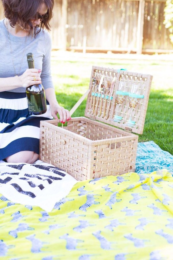 a woman sitting on the grass with a basket and bottle in front of her,