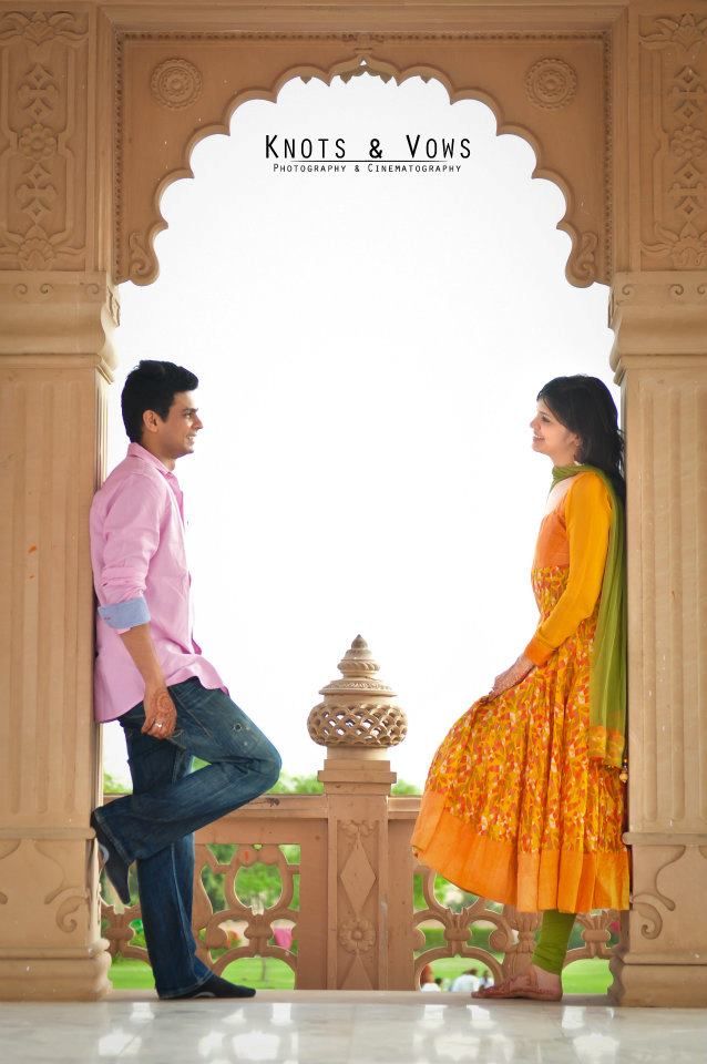 a man and woman standing next to each other in front of a wall with an archway