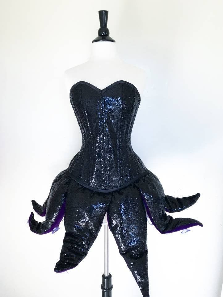 a black corset with purple sequins on the bust and bottom, sitting on a mannequin