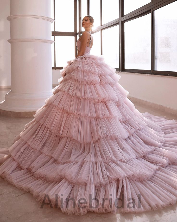 a woman in a long pink dress standing next to a window with large columns and windows behind her