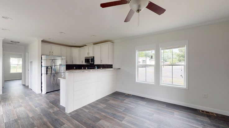 an empty kitchen and living room with wood flooring in the middle is seen from across the room