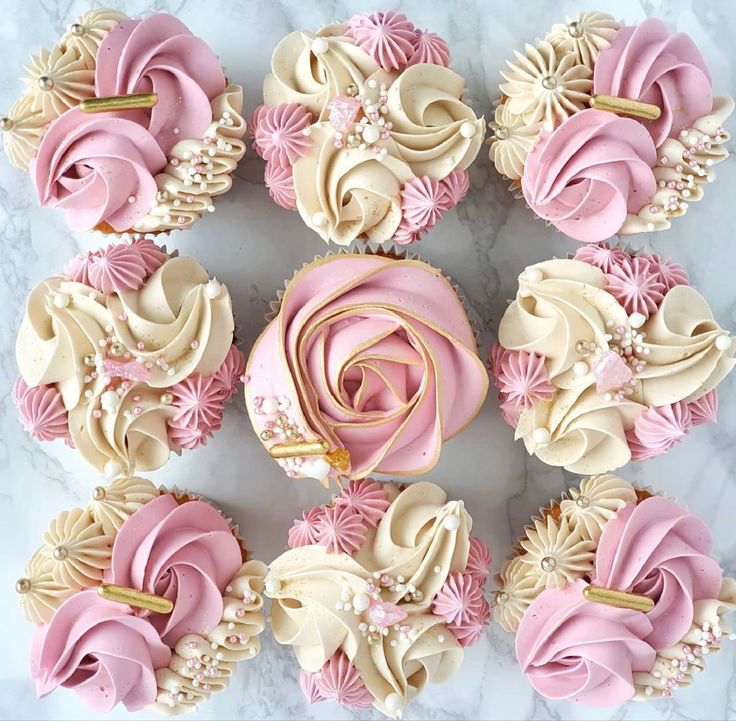 cupcakes decorated with pink and white icing on a marble table top next to each other