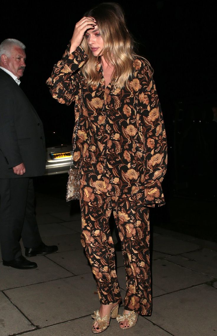 a woman is standing on the sidewalk at night with her hand in her hair and wearing floral clothing