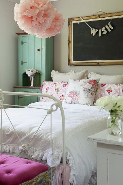 a white bed sitting under a pink flower on top of a wooden table next to a chalkboard