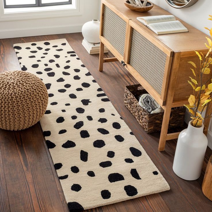 a white and black rug on the floor next to a wooden table with vases