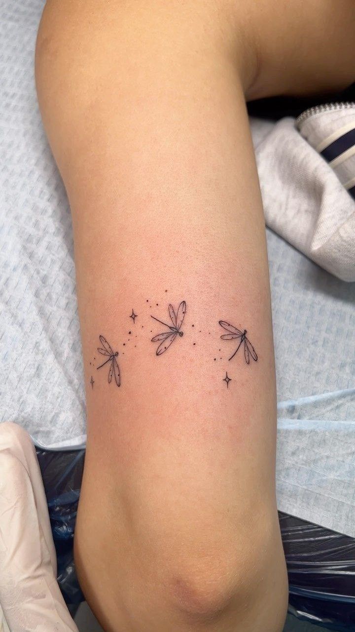 a woman's leg with three dragonflies tattoo on her left arm and two stars in the middle