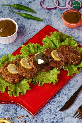 a red plate topped with meat covered in lettuce next to sauces and spoons