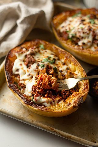 two stuffed sweet potatoes with meat and cheese on a baking sheet, one has a fork in it