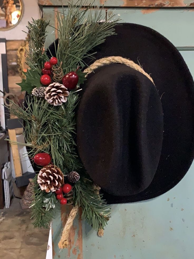 a black hat with pine cones and red berries hangs on a blue wall in a shop