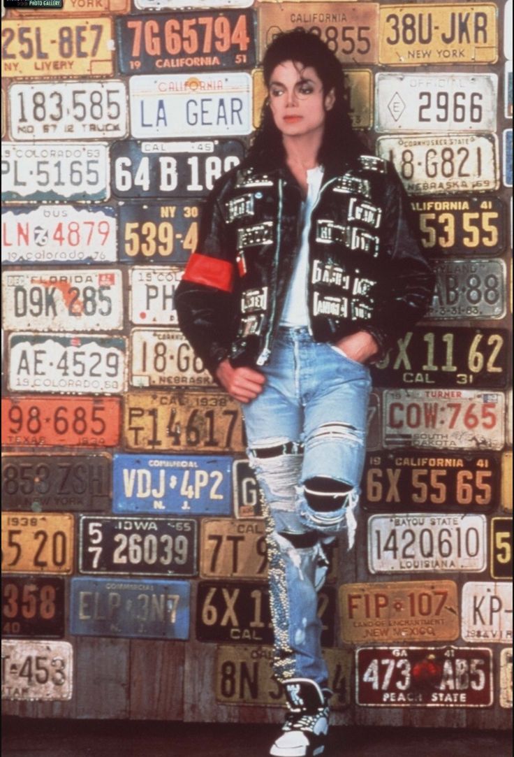 a man standing in front of a pile of license plates with his hands on his hips